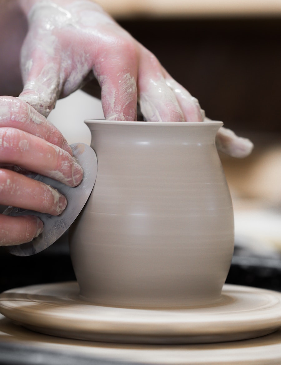 A student's hands pulling up the wall of a clay pot